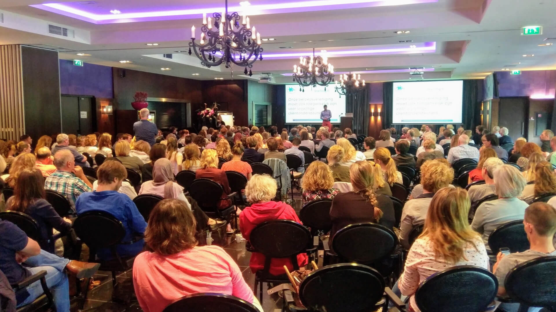 Een congreszaal vol met deelnemers die de Algemene Ledenvergadering bijwonen