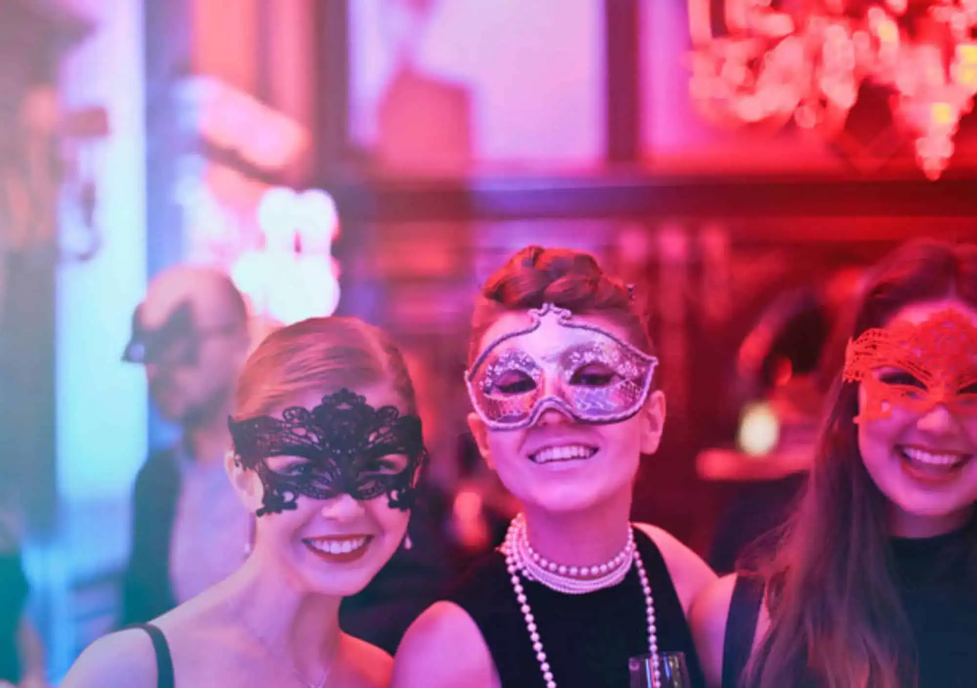 Drie stralende gasten dragen elegante kanten maskers tijdens een feestelijk evenement in een warm verlichte zaal.